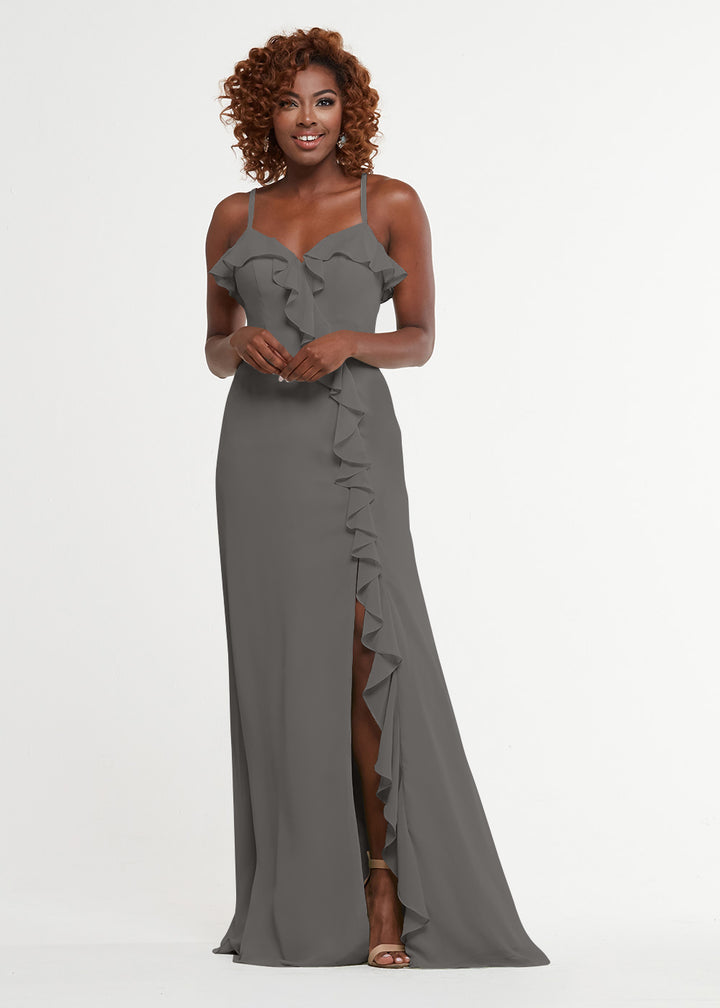 Smiling against a white background, a woman with curly hair wears Avery Austin style 80174—a long, sleeveless dress featuring thin straps, a ruffled sweetheart bodice, and a thigh-high ruffled slit.