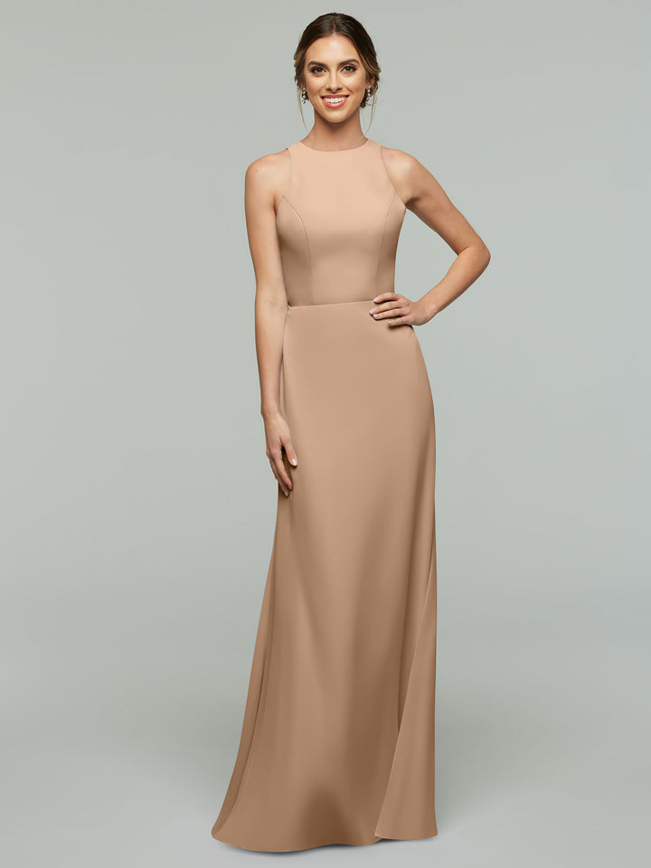 A woman smiles in Avery Austin’s 80175, a sleeveless, buff, floor-length A-line dress with a fitted bodice and high neckline, standing against a plain light gray background.