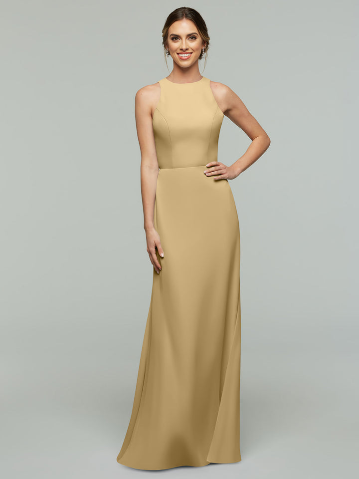 A woman models Avery Austin’s sleeveless, floor-length 80175 A-Line dress in champagne with a subtle V-neck, posing against a light gray background and smiling with one hand on her hip.