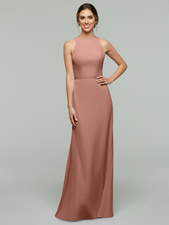 A woman smiles with one hand on her hip, wearing Avery Austin's floor-length, sleeveless A-Line dress (80175) in rose with a V-neck, standing against a plain gray background.