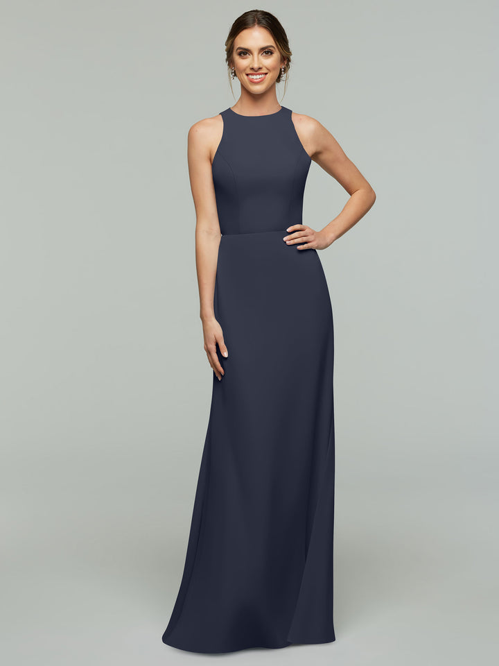 A woman smiles in Avery Austin’s 80175 dress—an elegant, long navy A-line with a fitted waist, high neckline, and subtle keyhole back—set against a plain light gray background.