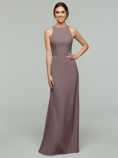 A woman stands smiling against a plain light gray background wearing Avery Austin’s 80175, a sleeveless floor-length mauve A-line dress, with one hand on her hip.
