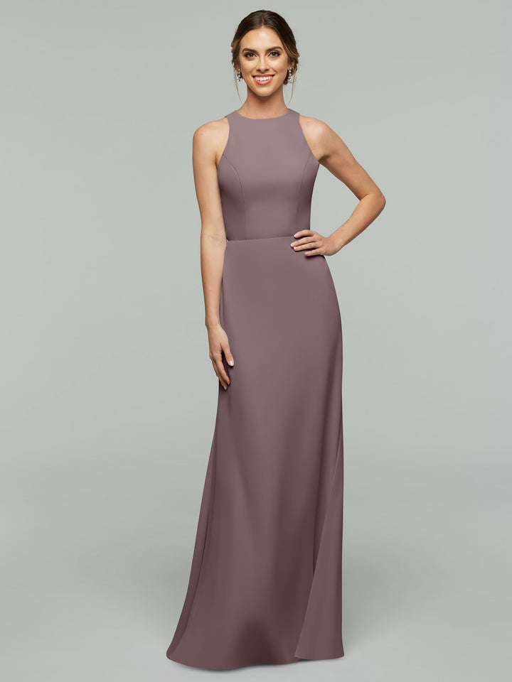 A woman stands smiling against a plain light gray background wearing Avery Austin’s 80175, a sleeveless floor-length mauve A-line dress, with one hand on her hip.