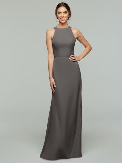 A woman smiles, wearing Avery Austin’s 80175—a sleeveless, floor-length A-line dress in dark gray with a fitted bodice and high neckline. The background is plain light gray.