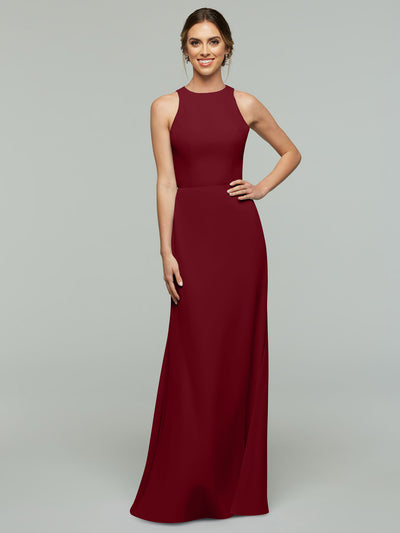 A woman smiles, wearing the Avery Austin 80175—a sleeveless, floor-length burgundy A-line dress with a high neckline. Her hair is tied back and one hand rests on her hip against a plain light gray background.