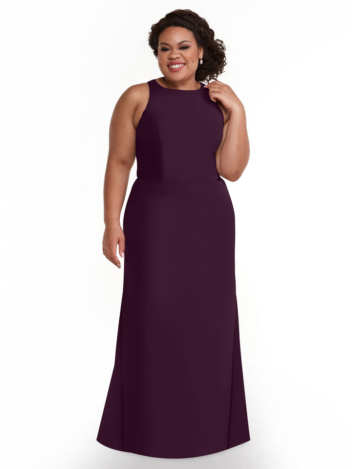 A woman with curly hair smiles against a plain white background wearing Avery Austin’s 80175, a sleeveless, floor-length A-line dress in aubergine.