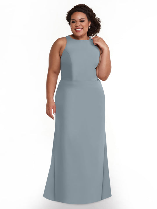 A woman with curly hair smiles against a white background, wearing Avery Austin’s floor-length, sleeveless light blue-gray A-line dress (style 80175) featuring a V-neck.