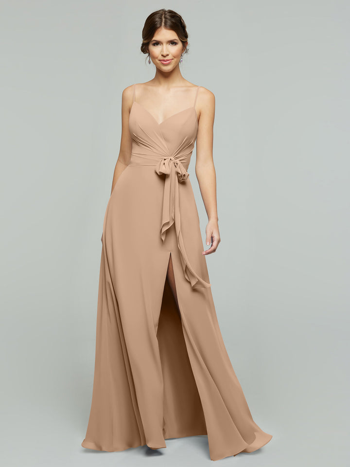 A woman wears the averyaustin 80182 light brown V-neck A-line chiffon dress with thin straps, fitted bodice, tied waist sash, and side slit, standing against a plain gray background.