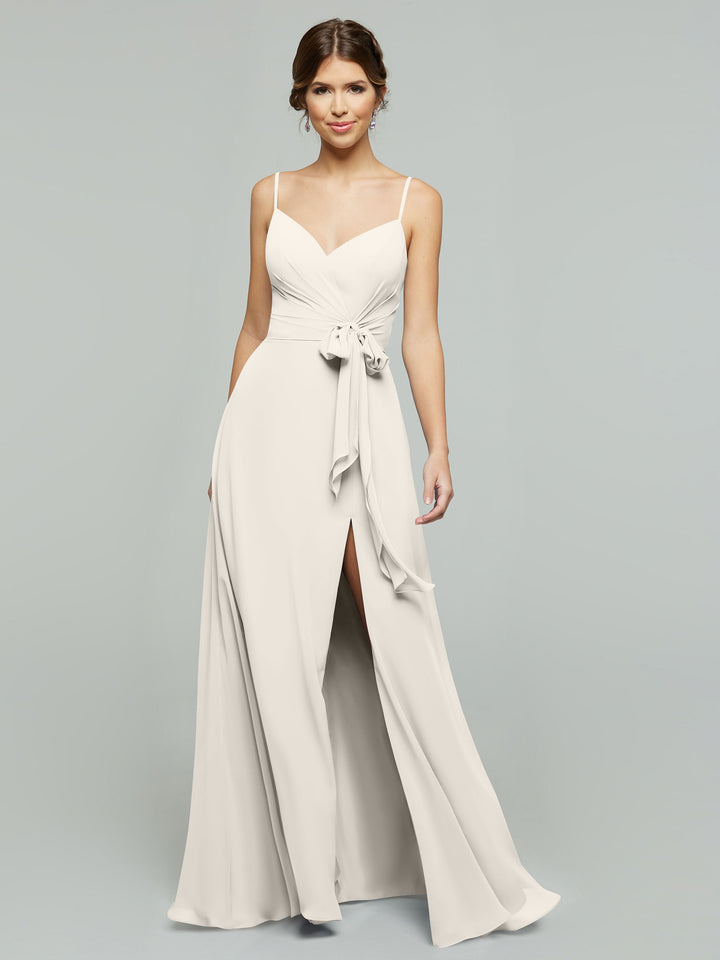 A woman models the averyaustin 80182: a long, light beige chiffon V-neck dress with thin straps, side slit, and waist ribbon, standing against a plain light gray background.