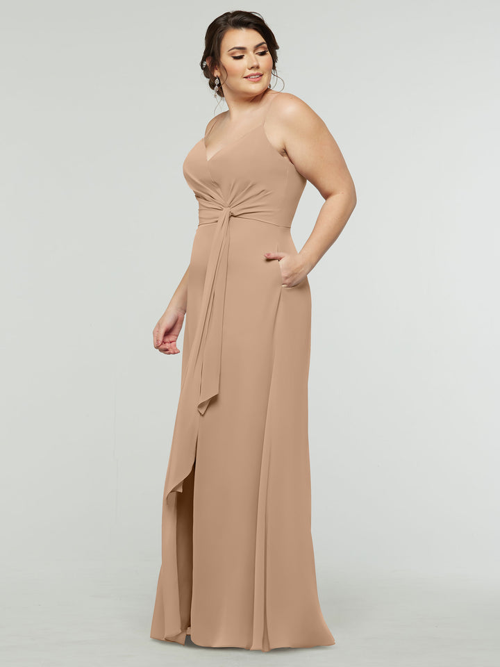 A woman models averyaustin’s 80182—a sleeveless, floor-length tan A-line chiffon dress with a V-neck, knotted waist, side pockets, and subtle slit—posing against a plain light background and gazing to the side with a gentle smile.