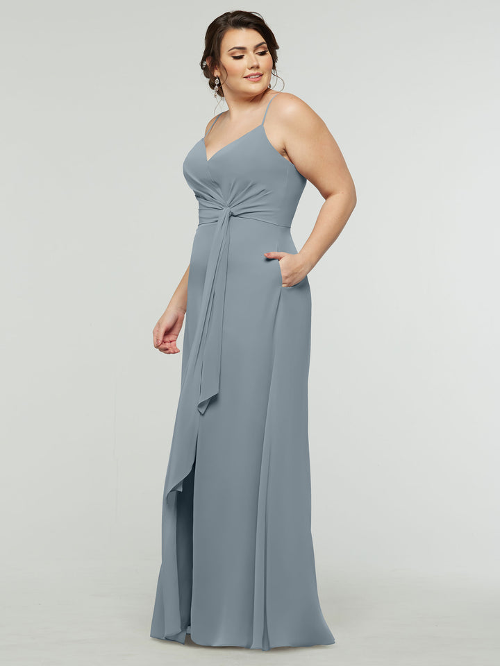 A woman wears the averyaustin 80182, a sleeveless, floor-length A-line chiffon dress with a V-neck and ruched bodice, standing against a plain light background and smiling slightly to the side.
