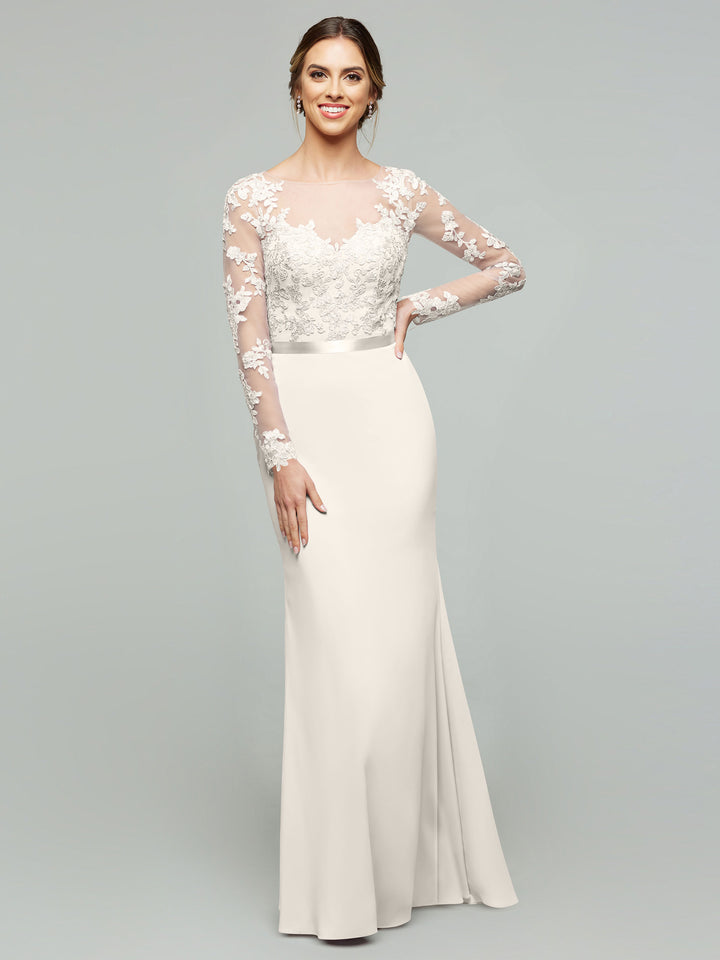 A woman models averyaustin style 80190, a long fitted white chiffon mermaid dress featuring a lace bodice and illusion lace sleeves, smiling against a plain light gray background.