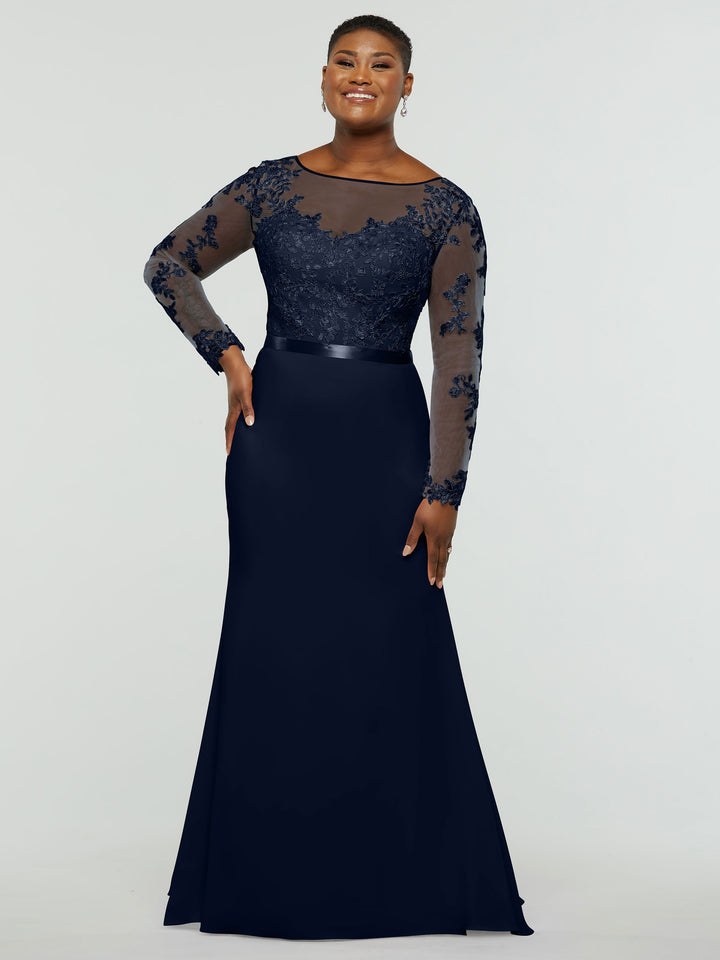 A woman smiles in the averyaustin TH-80190 midnight dress, featuring a lace bodice, illusion lace sleeves, satin waistband, and floor-length chiffon mermaid skirt. She stands against a plain light background.