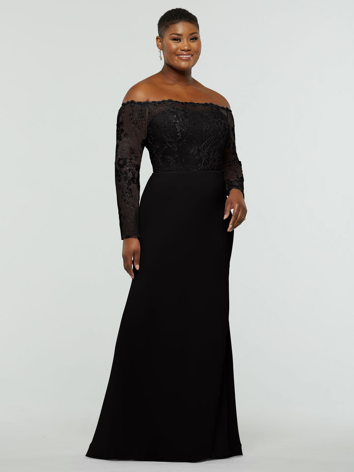 A woman wearing averyaustin’s 80191 black gown with a lace bodice, lace sleeves, off-the-shoulder neckline, and fitted silhouette stands smiling against a light gray background.