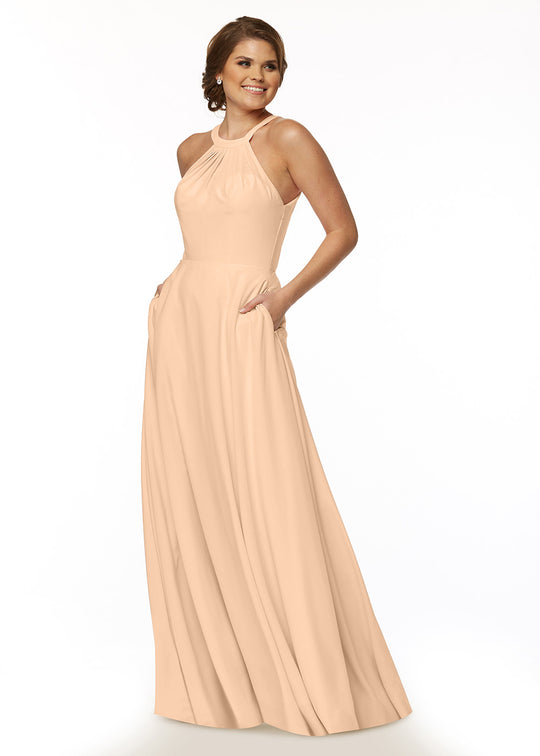 A woman smiles, wearing Avery Austin’s 83002: a peach floor-length A-line dress featuring a high neckline, subtle top pleats, and pockets. Her hair is styled in a low updo.