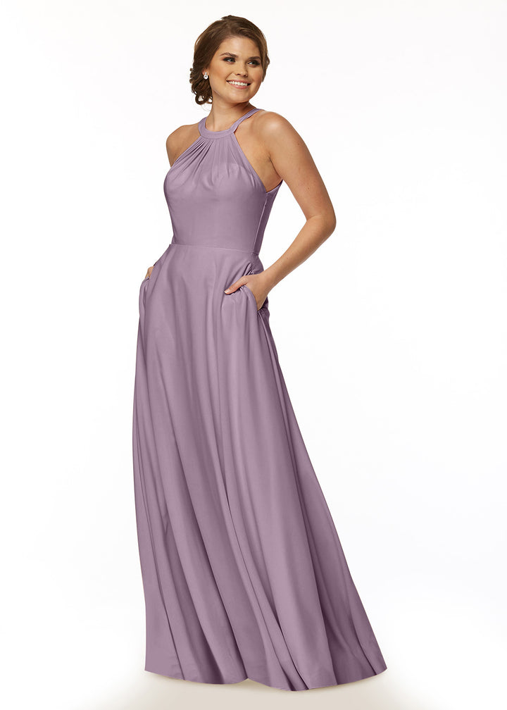A woman smiles in the Avery Austin 83002, a sleeveless, floor-length lavender A-Line dress with a halter neck and pockets, set against a plain white background.