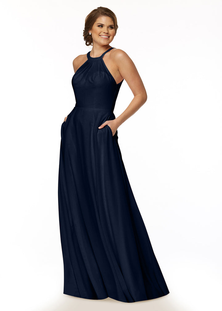 A woman smiles in the Avery Austin 83002—a sleeveless, floor-length navy blue A-Line dress with a high neckline and pockets—set against a plain white background.