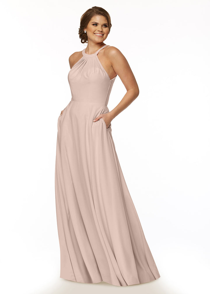 A woman in the Avery Austin 83002 A-Line sleeveless, floor-length rose pink gown with a high neckline and side pockets stands against a white background, smiling.