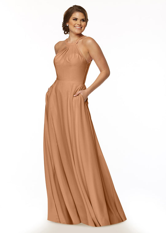 A woman in Avery Austin’s 83002—a sleeveless, floor-length A-line halter dress with a flowy skirt—smiles with her hands in her pockets against a plain white background.