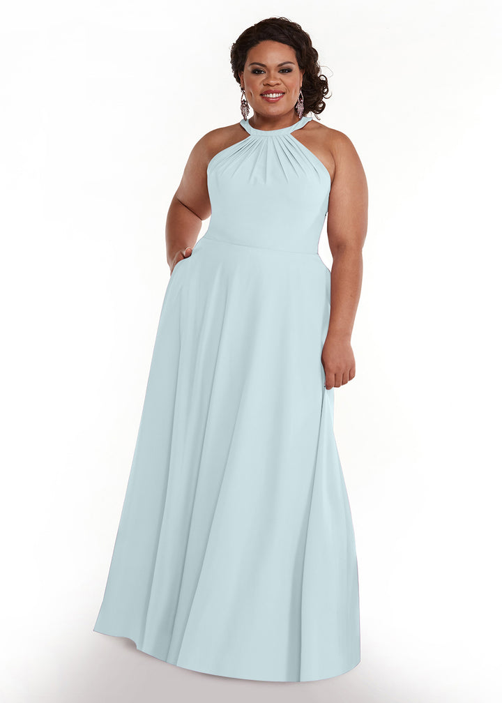 A woman with curly hair and statement earrings smiles with one hand in her pocket, wearing Avery Austin style 83002: a light blue, floor-length, sleeveless halter neck A-line dress, on a white background.