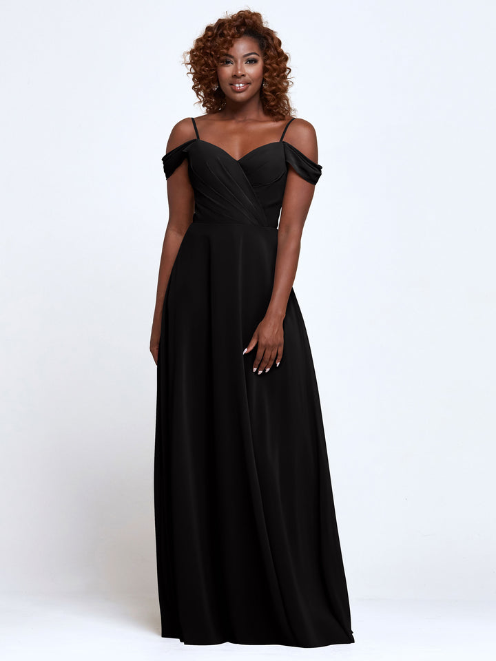 A woman with curly hair smiles in Avery Austin’s 83003—a floor-length, off-the-shoulder bridesmaid dress featuring thin straps and a fitted bodice—posing against a plain white background.