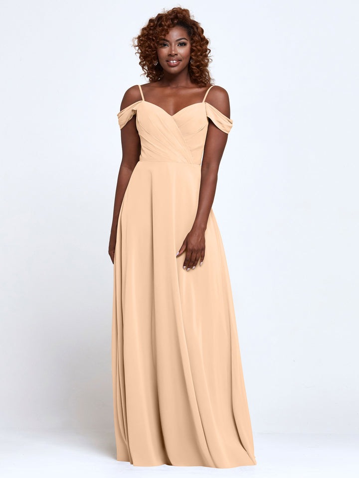 A woman wears the Avery Austin TH-83003 bridesmaid dress in blush, standing against a white background and smiling with her arms relaxed at her sides.