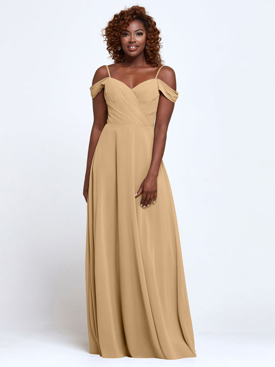 A woman with curly hair models Avery Austin's 83003: a light gold, off-the-shoulder bridesmaid dress with thin straps and a flowing skirt, set against a plain white background.