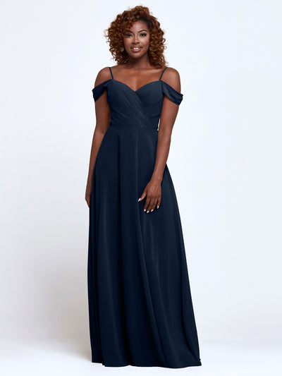 A woman wears Avery Austin’s 83003, a navy blue, floor-length, off-the-shoulder bridesmaid dress with thin straps, smiling against a plain white background.