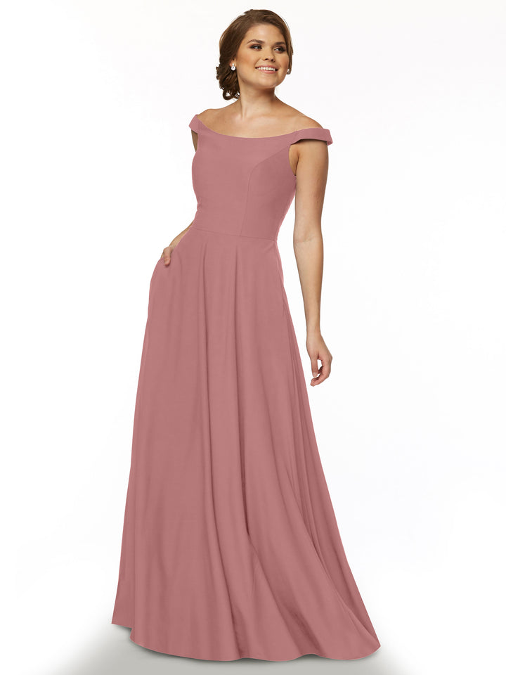 A woman smiles with her hair styled back, wearing the Avery Austin TH-83005 dress in Dusty Rose—a flowing, off-the-shoulder gown with a straight across neckline—posed against a plain white background.