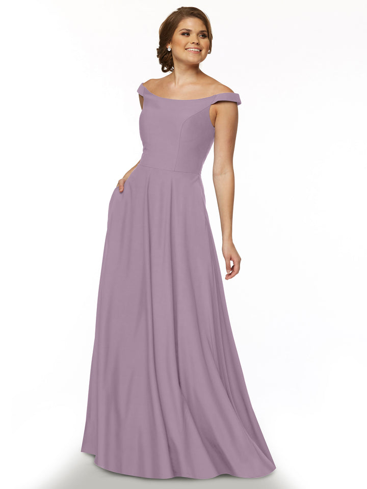 A woman stands and smiles against a white background wearing Avery Austin style 83005, a floor-length lavender dress featuring an off-the-shoulder neckline, fitted bodice, and flowing skirt.