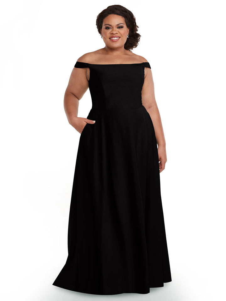 A woman models Avery Austin 83005, a black floor-length, off-the-shoulder dress with a straight across neckline, posing against a white background and smiling with one hand in her pocket to highlight the shoulder detail.