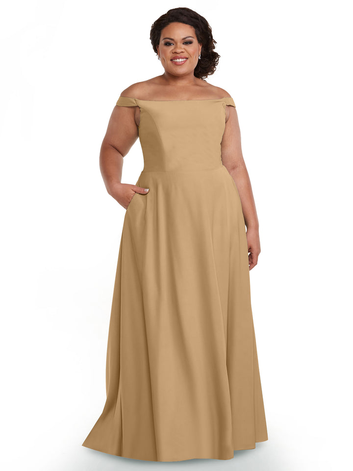 A woman smiles in the Avery Austin 83005, a floor-length off-the-shoulder gown with a straight neckline and pockets, shown here in Cappuccino against a plain white background.