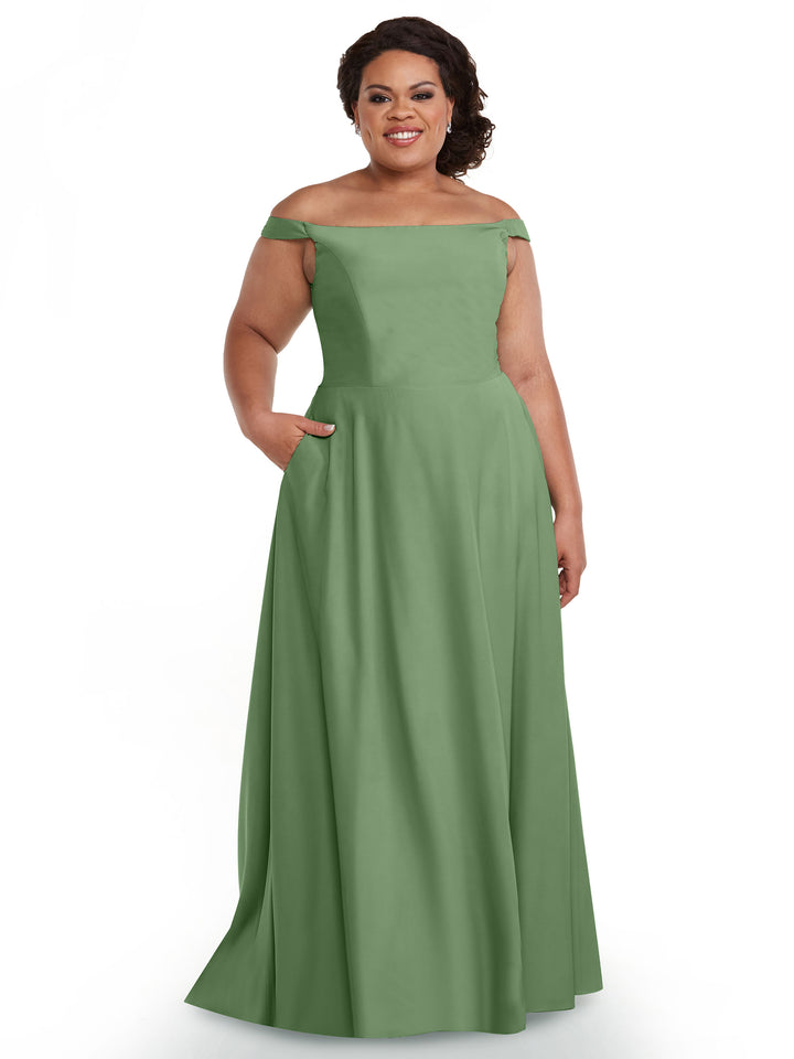 A woman stands smiling against a white background, wearing the Avery Austin TH-83005 floor-length dress in dusty sage with pockets, featuring a straight across, off-the-shoulder neckline that highlights her shoulders.