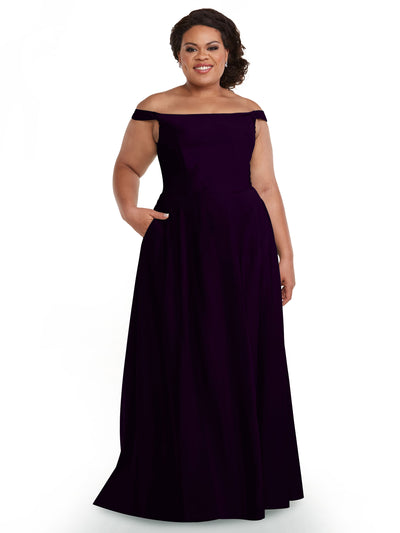 A woman smiles wearing Avery Austin's 83005, a floor-length, off-the-shoulder dress with a straight-across neckline and pockets, as she poses against a plain white background.