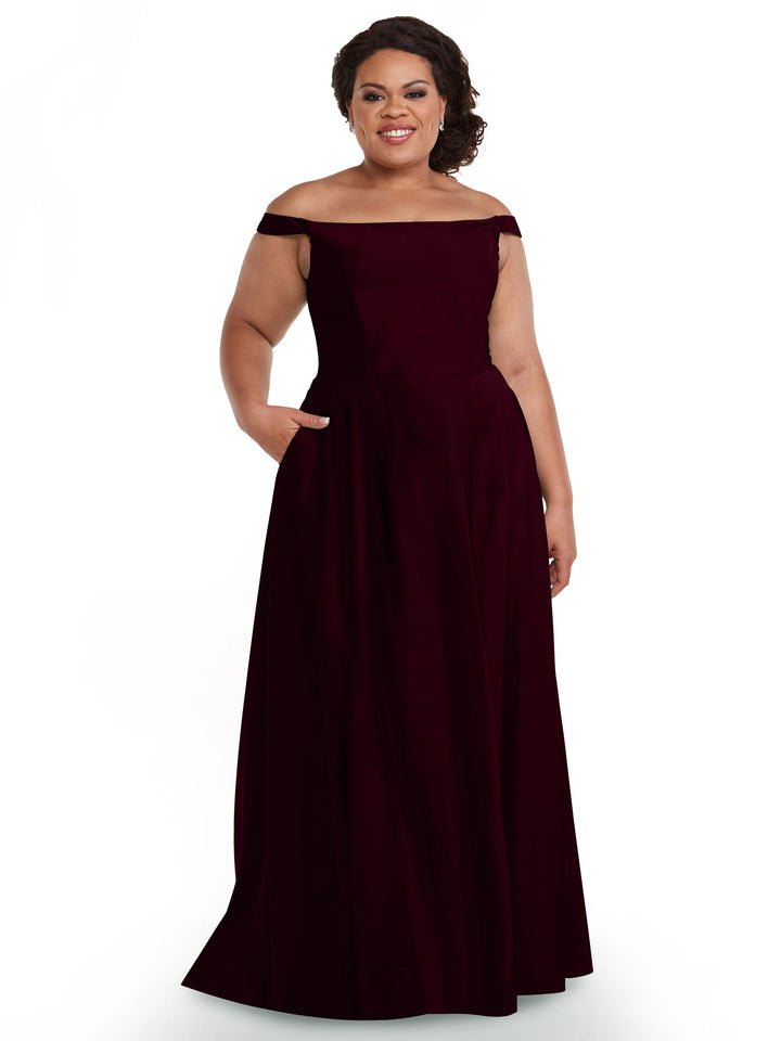 A woman wearing the Avery Austin 83005 dress in maroon with an off-the-shoulder, straight neckline and pockets stands smiling against a plain white background.