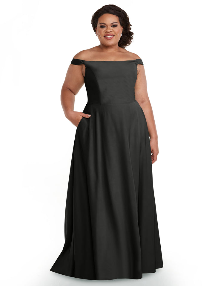 A woman smiles in the Avery Austin 83005, a steel gray off-the-shoulder gown with a straight neckline and pockets. The floor-length dress elegantly highlights her shoulders as she poses against a simple white background.
