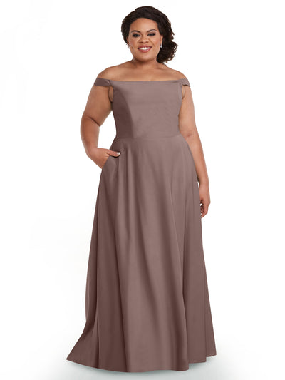 A woman smiles in the Avery Austin 83005, a mauve, floor-length off-the-shoulder dress with a straight-across neckline and pockets, posing against a white background.