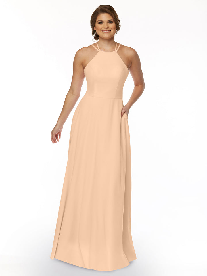 A woman smiles in Avery Austin’s 83006, a sleeveless, light peach A-line dress with a halter neckline and fitted bodice. The flowing skirt drapes elegantly against a plain white background.