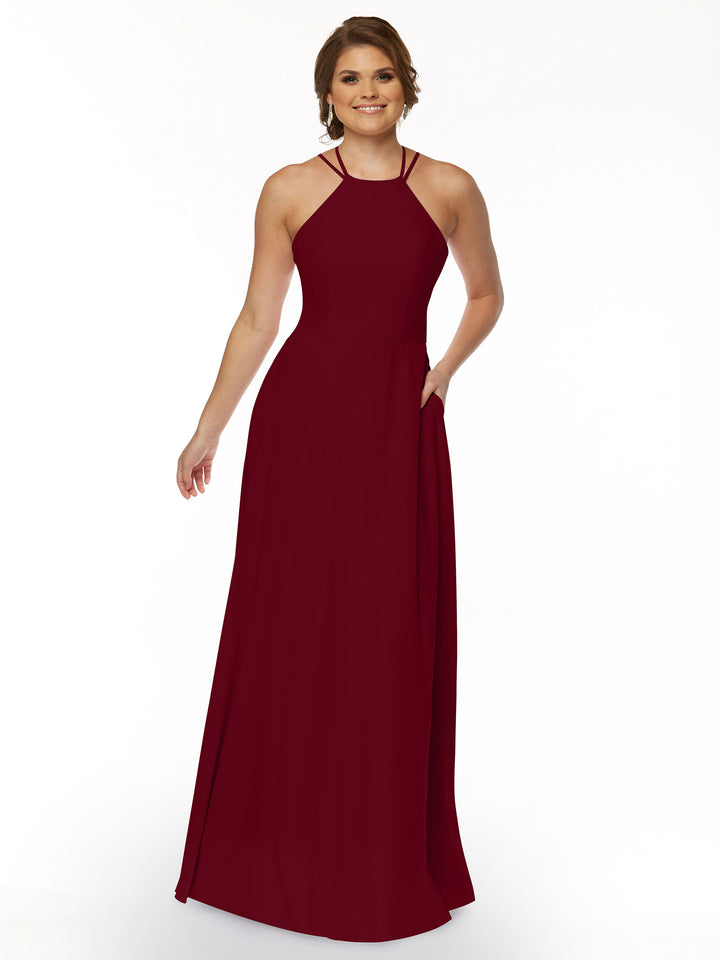 A woman smiles against a white background wearing Avery Austin’s 83006—a sleeveless, floor-length, burgundy A-line dress with a halter neckline, thin straps, and pockets.