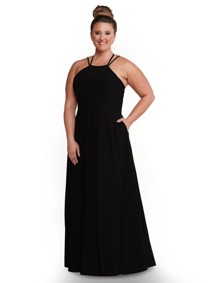 A woman with her hair in a bun models Avery Austin’s 83006: a sleeveless, floor-length black A-line dress with thin straps, standing and smiling lightly against a plain white background.