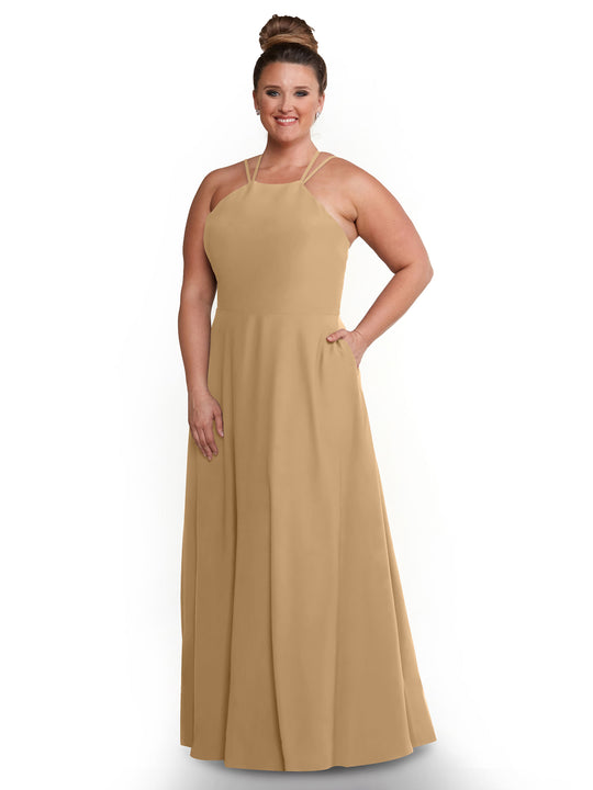 A woman in Avery Austin’s 83006 tan A-line dress with a halter neckline stands smiling, one hand on her hip and the other in her pocket, against a white background.