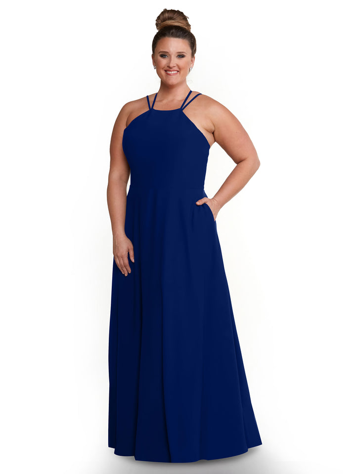 A woman stands smiling with one hand in her pocket, wearing the Avery Austin 83006 royal blue sleeveless A-Line floor-length dress with double shoulder straps, set against a plain white background.