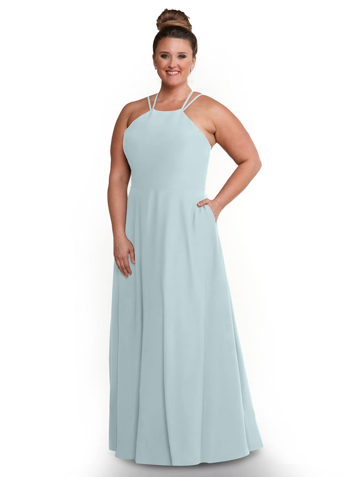 A woman with her hair in a high bun smiles against a white background, wearing Avery Austin style 83006—a light blue, floor-length A-line dress with a halter neckline and pockets.
