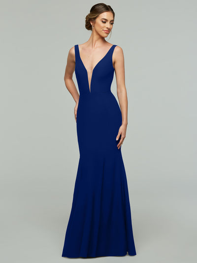 A woman in the Avery Austin 83010, a sleeveless floor-length cobalt gown with a plunging neckline, stands against a plain gray background, smiling softly and looking to the side.