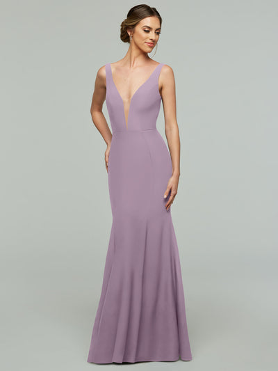 A woman models Avery Austin's 83010, an elegant sleeveless floor-length lavender mermaid dress with a plunging neckline, against a plain gray background, posing confidently.