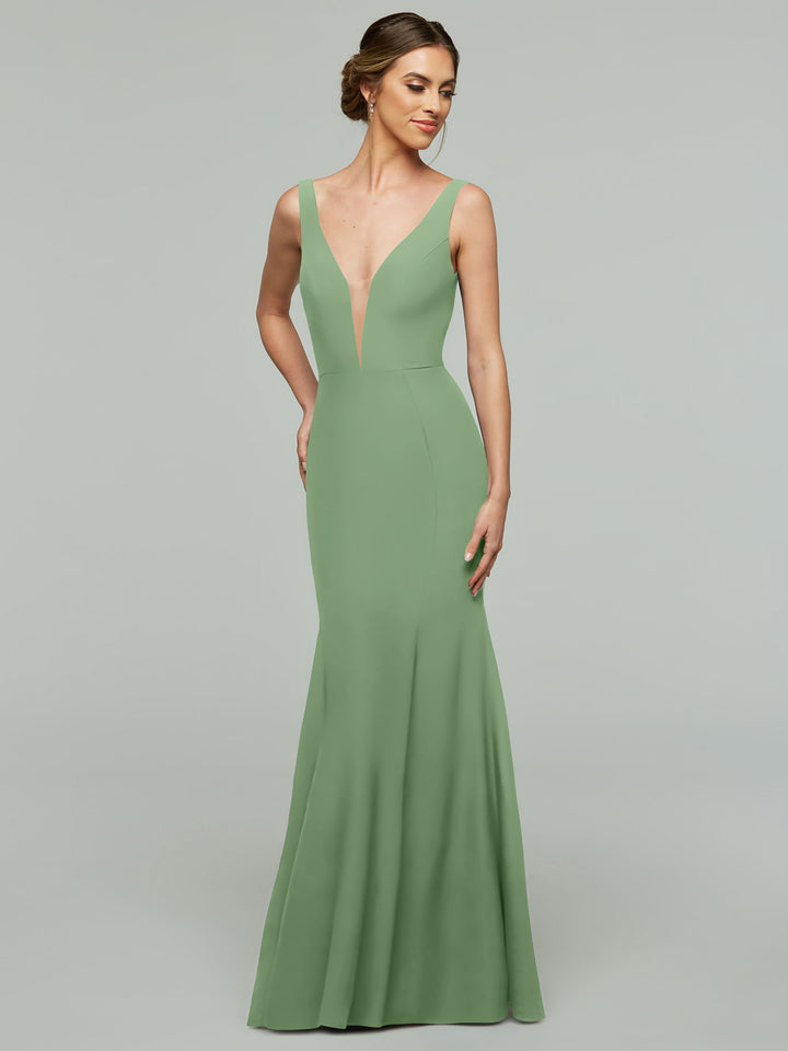 An elegant woman poses against a plain light gray background, wearing Avery Austin’s 83010 dress in Dusty Sage: a sleeveless, floor-length mermaid gown with a plunging neckline and fitted bodice.
