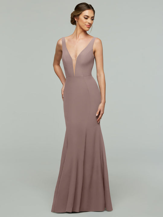 A woman in the Avery Austin 83010, a vintage mauve floor-length mermaid dress with a plunging neckline and fitted bodice, stands against a plain light gray background, looking to the side and smiling slightly.