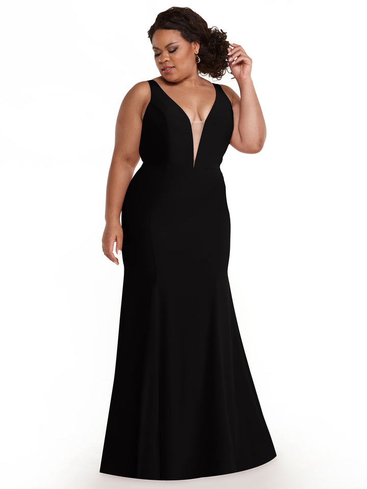 A woman in the Avery Austin 83010 black mermaid dress with a plunging neckline stands against a white background, looking down and touching her curled hair.