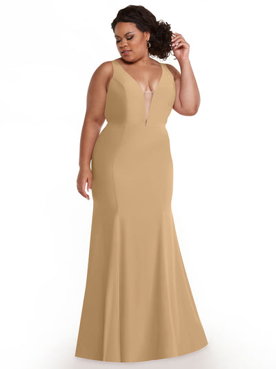 A woman poses against a white background, gently touching her hair while wearing Avery Austin’s 83010—a sleeveless, floor-length camel mermaid dress with a plunging neckline.