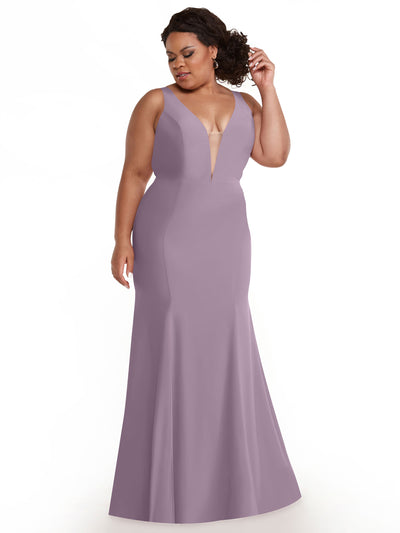 A woman models Avery Austin’s 83010, a floor-length dusty lavender mermaid gown with a plunging neckline and fitted bodice, standing against a white background and adjusting her hair.